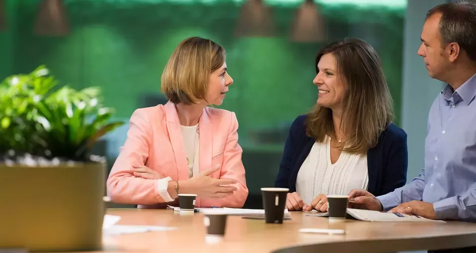  Three people engaged in conversation while seated at a table, sharing ideas and enjoying each other's company.