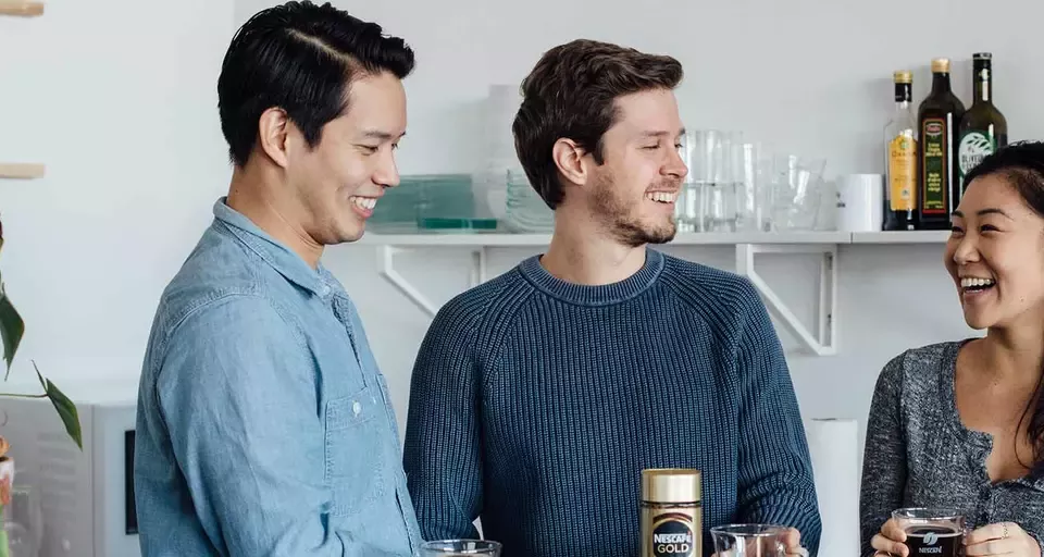 A table with three individuals, each holding a drink and sharing a lively discussion.