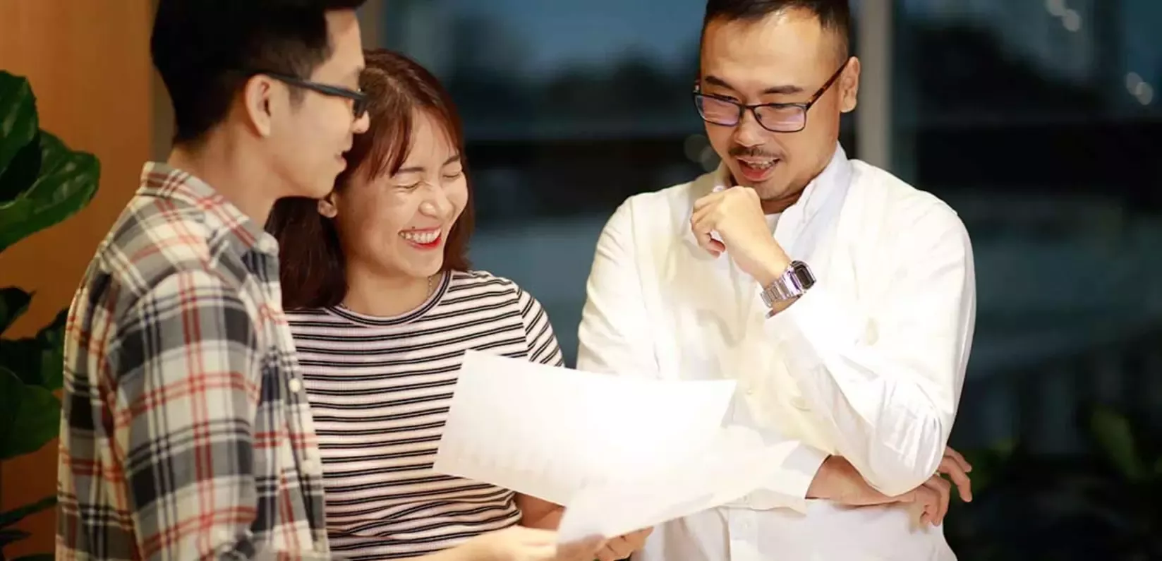 Three people are gathered around, examining a document on a table with focused expressions.