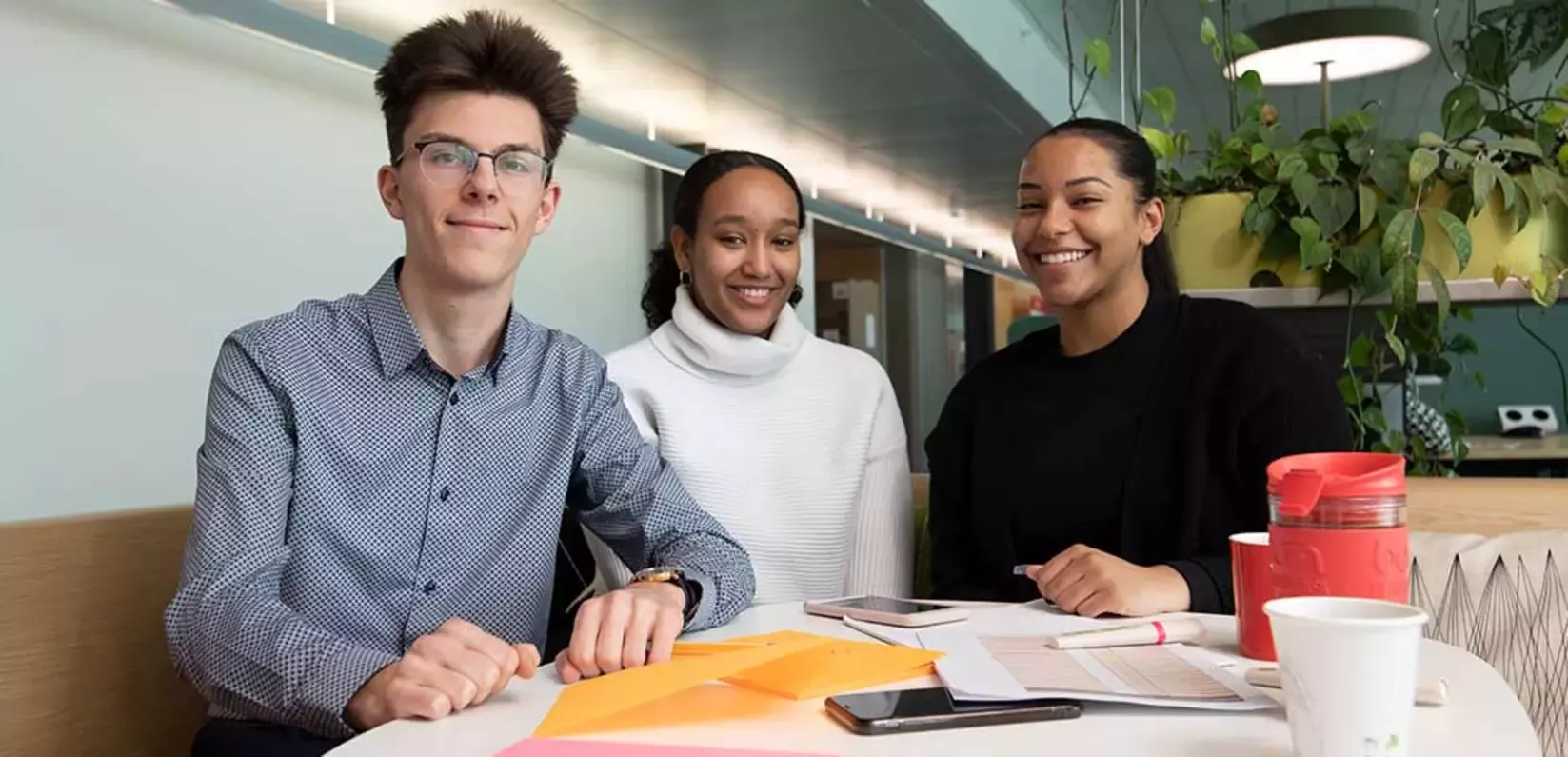 Three young people at a table, smiling happily and sharing ideas.