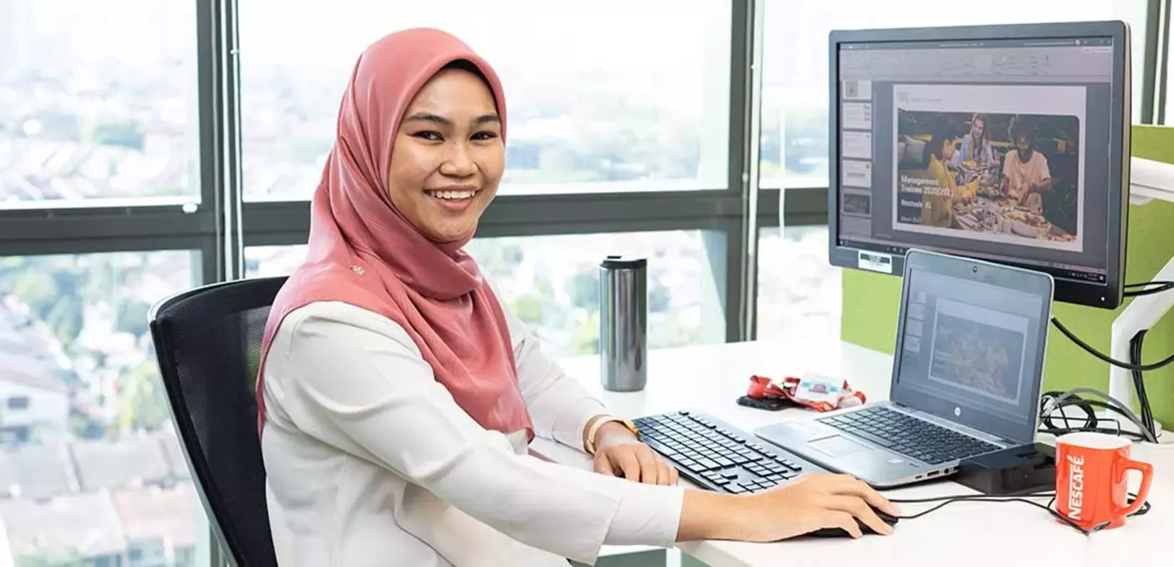A woman in a hijab is at her desk, focused on her laptop