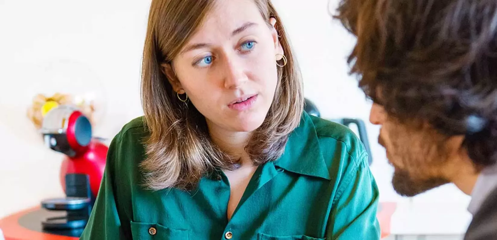 A woman with shoulder-length hair wearing a green shirt engages in conversation with a man