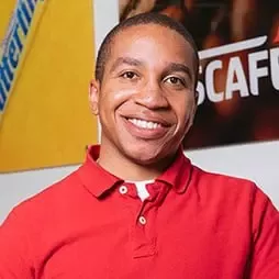 A man wearing a red shirt smiles warmly at the camera.
