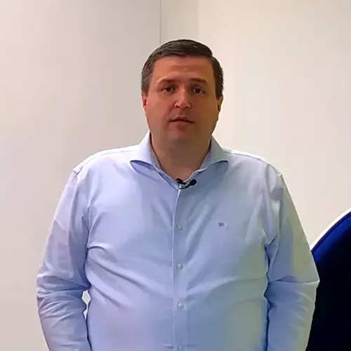 A man in a blue shirt stands against a wall