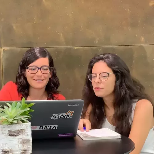 Two women seated at a table, collaborating on a laptop, engaged in discussion
