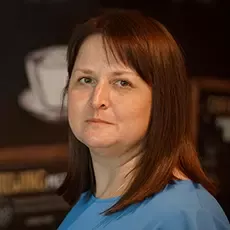 A woman dressed in a blue shirt stands against a wall