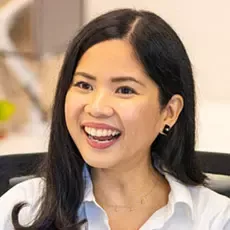 A woman with long, dark hair wearing a white shirt and earrings
